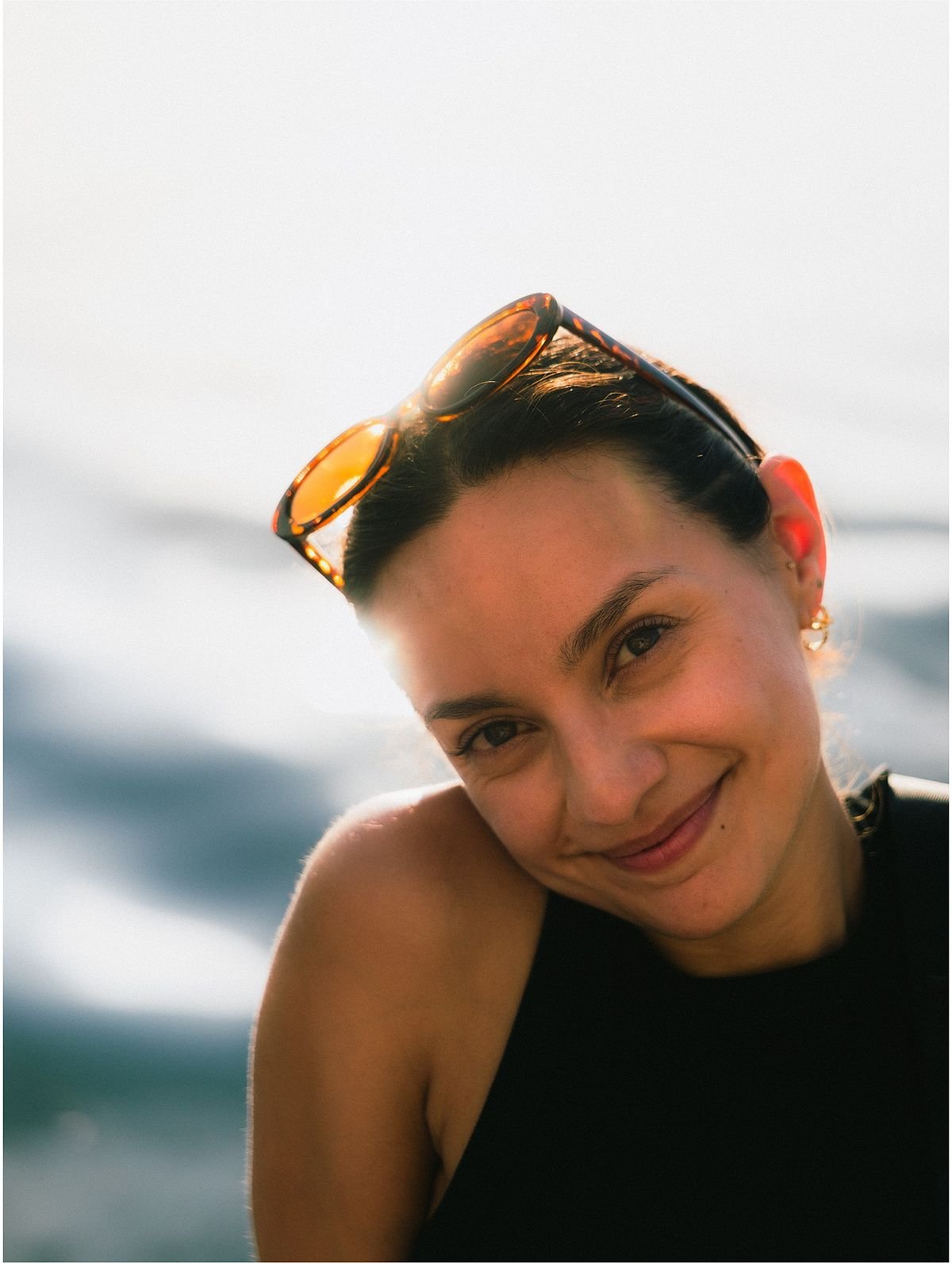 A woman with sunglasses pushed up on her head tilts her head and smiles at the camera.